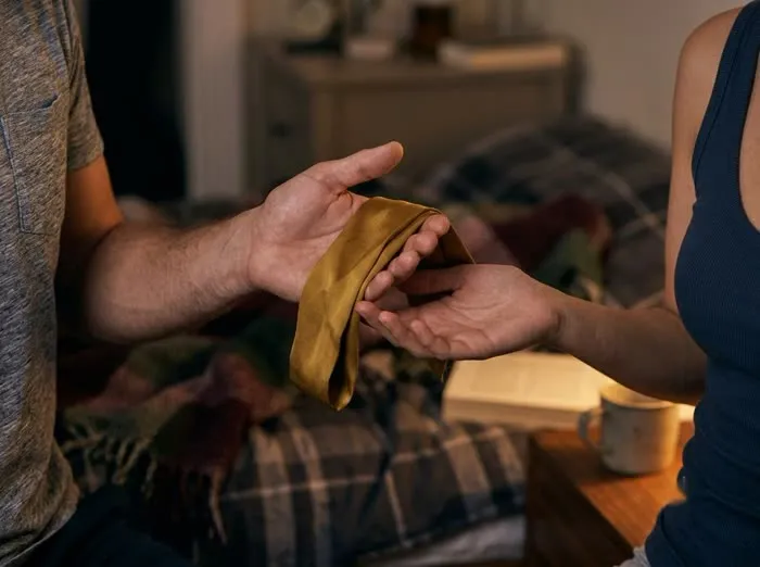 Manos de una pareja compartiendo una cinta de seda dorada, gesto de confianza y consentimiento