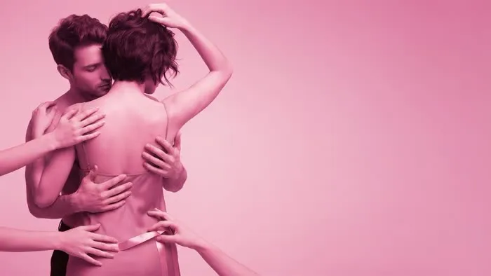 Pareja monogamish abrazada en tonos rosas, rodeada por las manos de otras personas