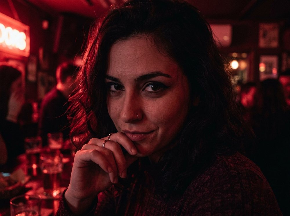 Retrato de mujer con mirada intensa y misteriosa bajo luz roja tenue en un bar nocturno