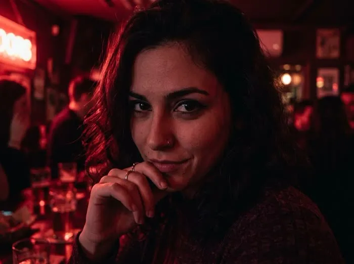 Retrato de mujer con mirada intensa y misteriosa bajo luz roja tenue en un bar nocturno